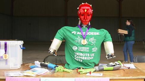Robot with red plastic head and green t shirt sitting at a conference desk